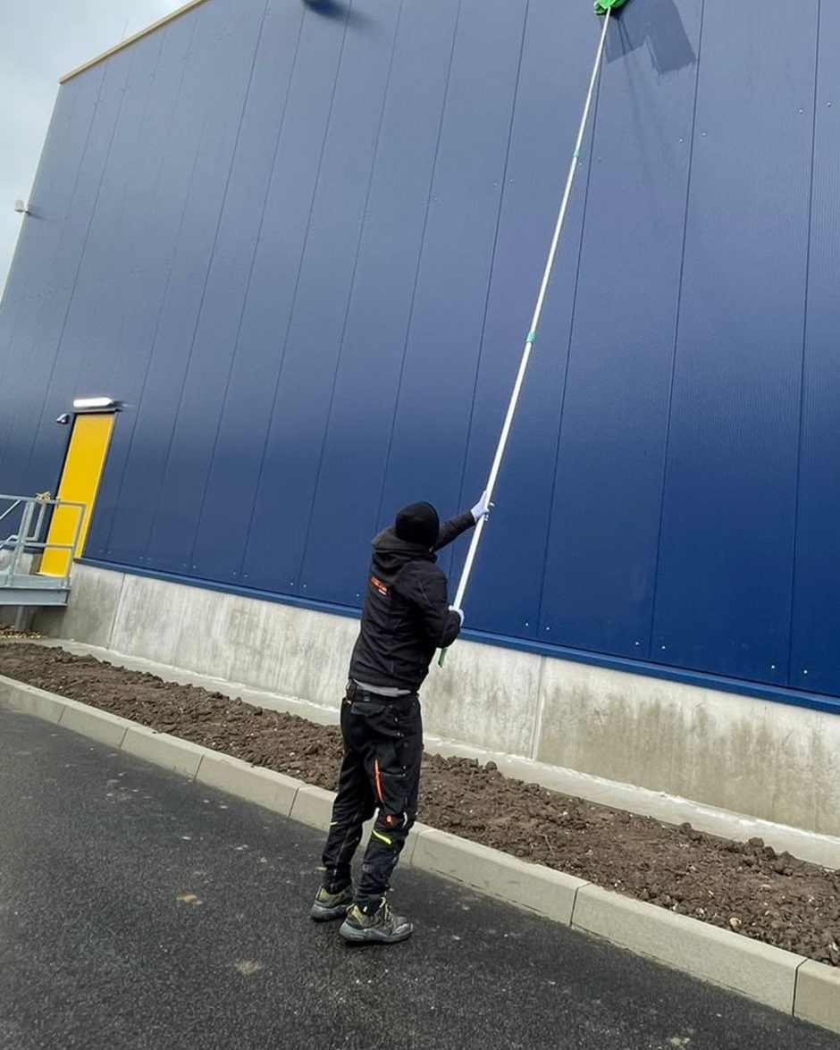 DICAM-Mitarbeiter reinigt mit einer Teleskopstange die Fassade einer Gewerbehalle